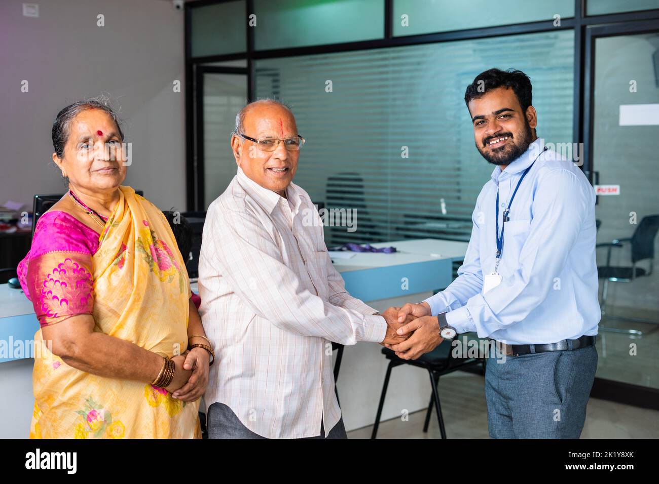 Happy smiling banker greeting by shaking hand to senior couple at bank - concept of financial support, banking adviser and consultation. Stock Photo