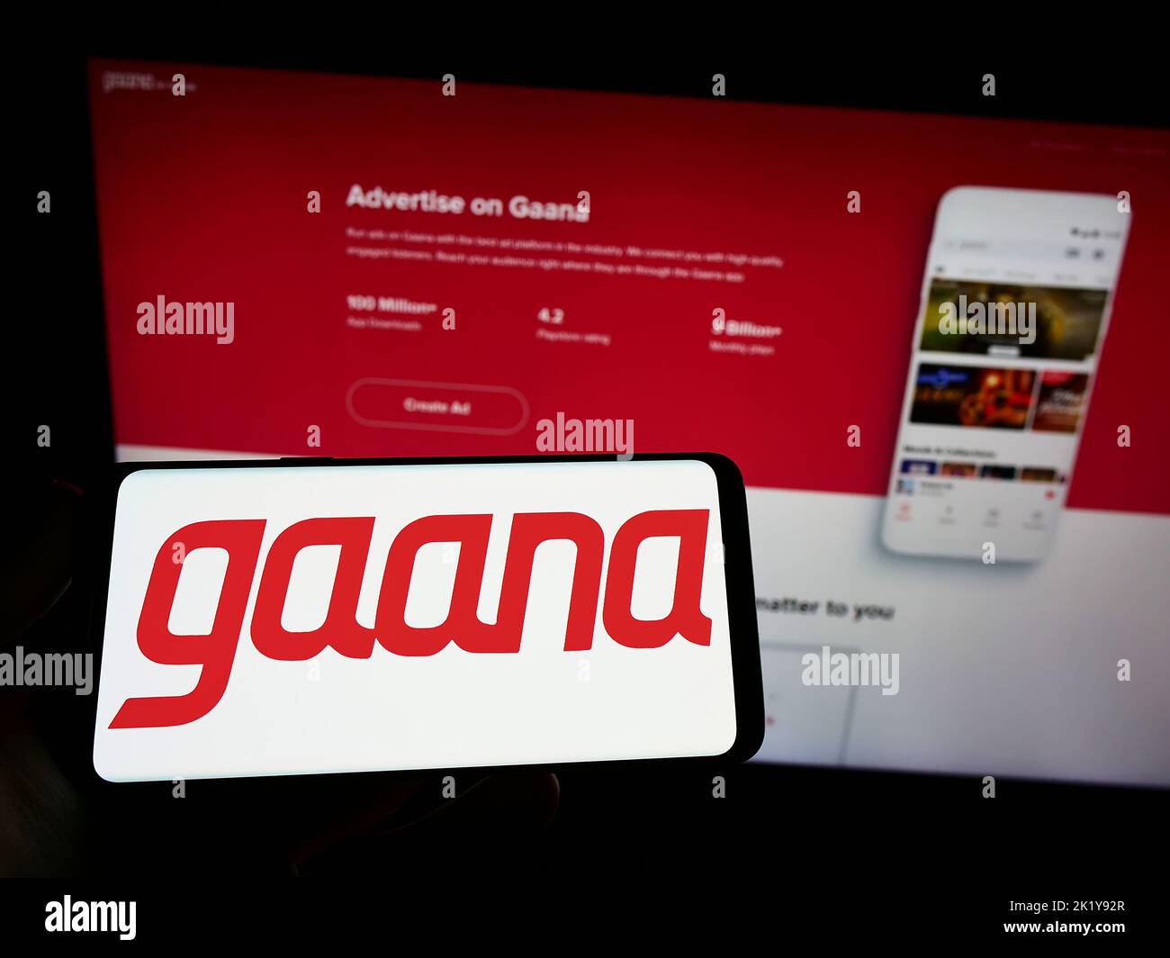 Person holding smartphone with logo of music streaming company Gamma Gaana Ltd. on screen in front of website. Focus on phone display. Stock Photo