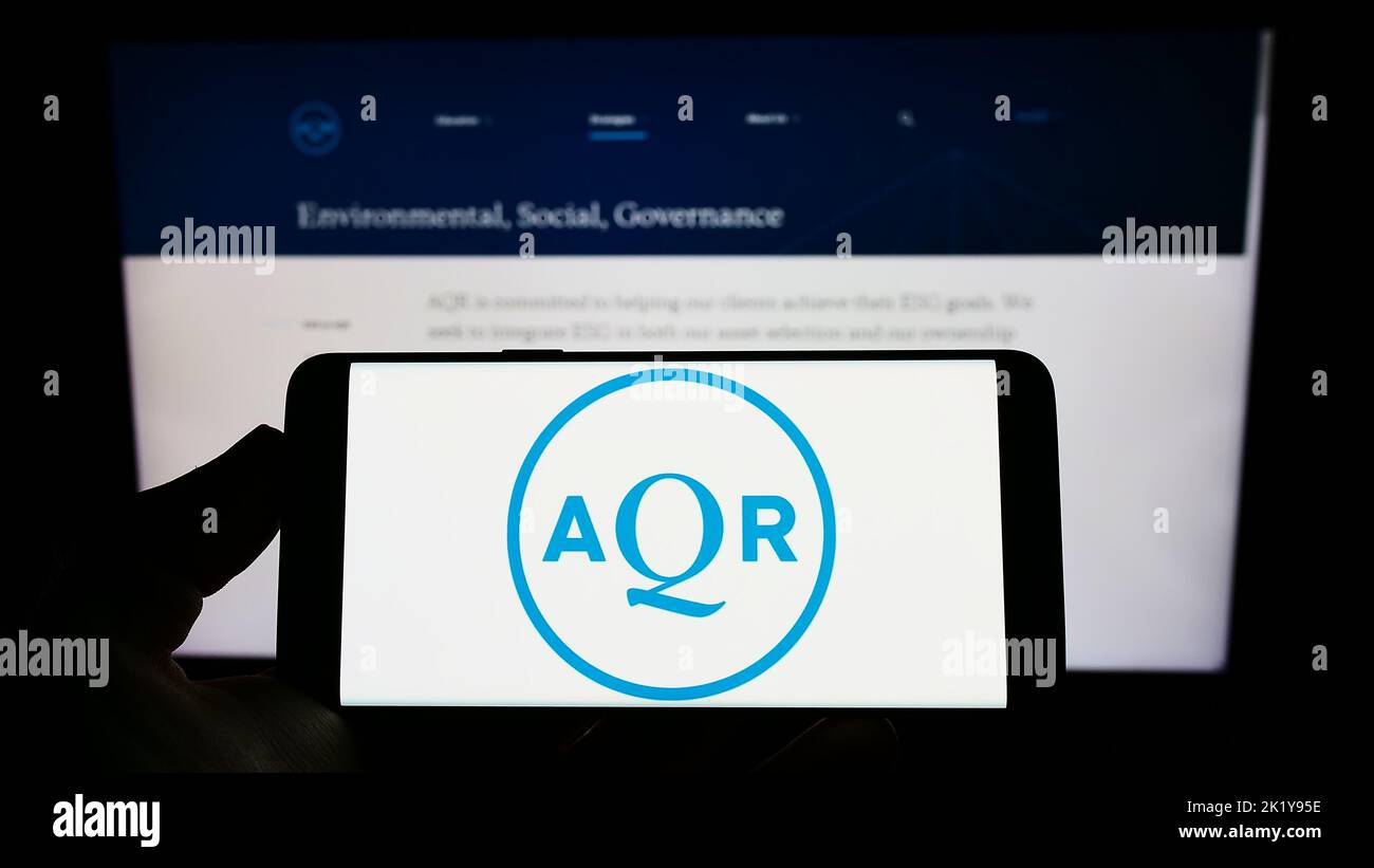Person holding smartphone with logo of US investment company AQR Capital Management on screen in front of website. Focus on phone display. Stock Photo