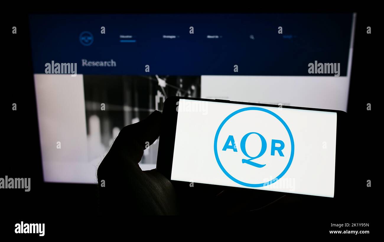 Person holding mobile phone with logo of American investment company AQR Capital Management on screen in front of webpage. Focus on phone display. Stock Photo