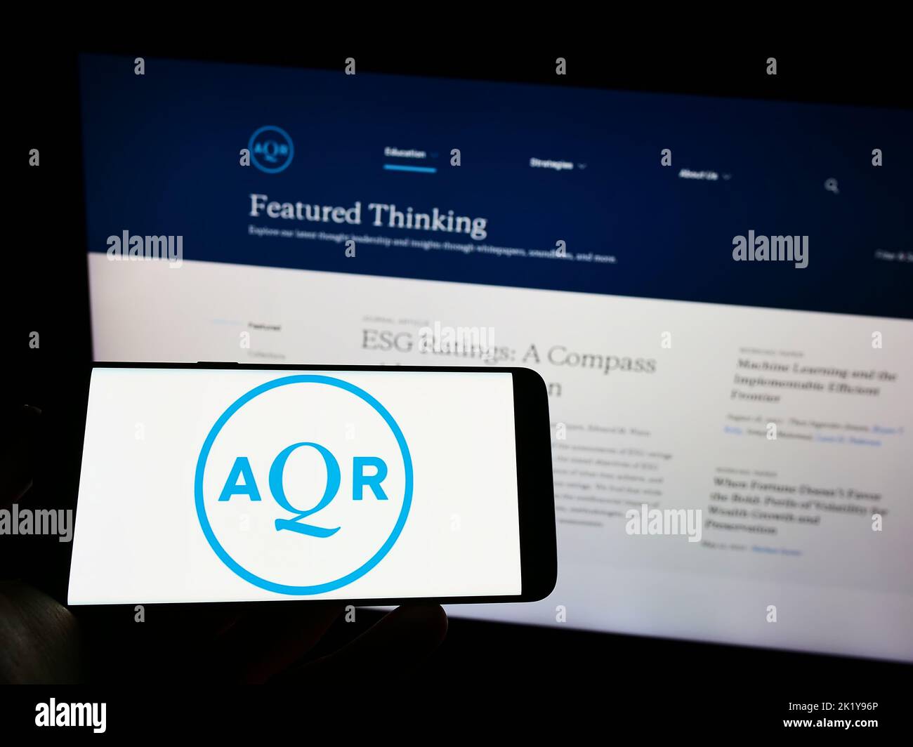 Person holding cellphone with logo of US investment company AQR Capital Management on screen in front of business web page. Focus on phone display. Stock Photo