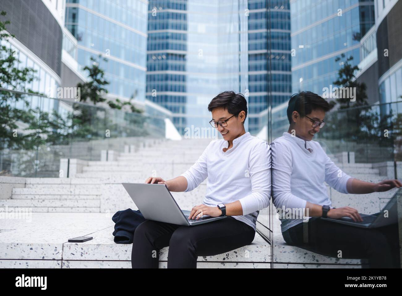 Young businessman sitting outdoors in the city working on laptop Stock Photo