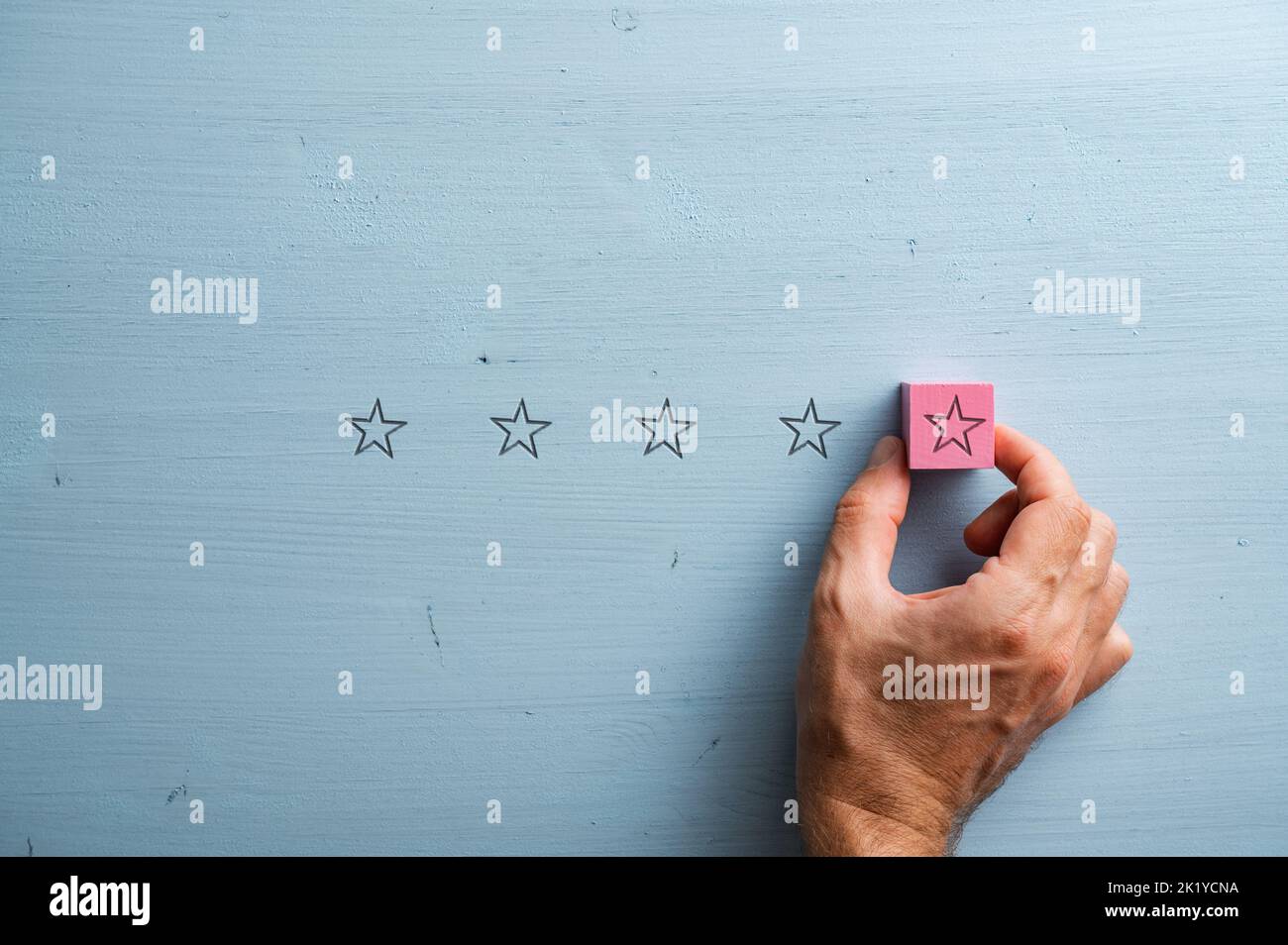 Male hand placing a pink wooden block with star shape on it in a line of five. Over pastel blue wooden background. Stock Photo