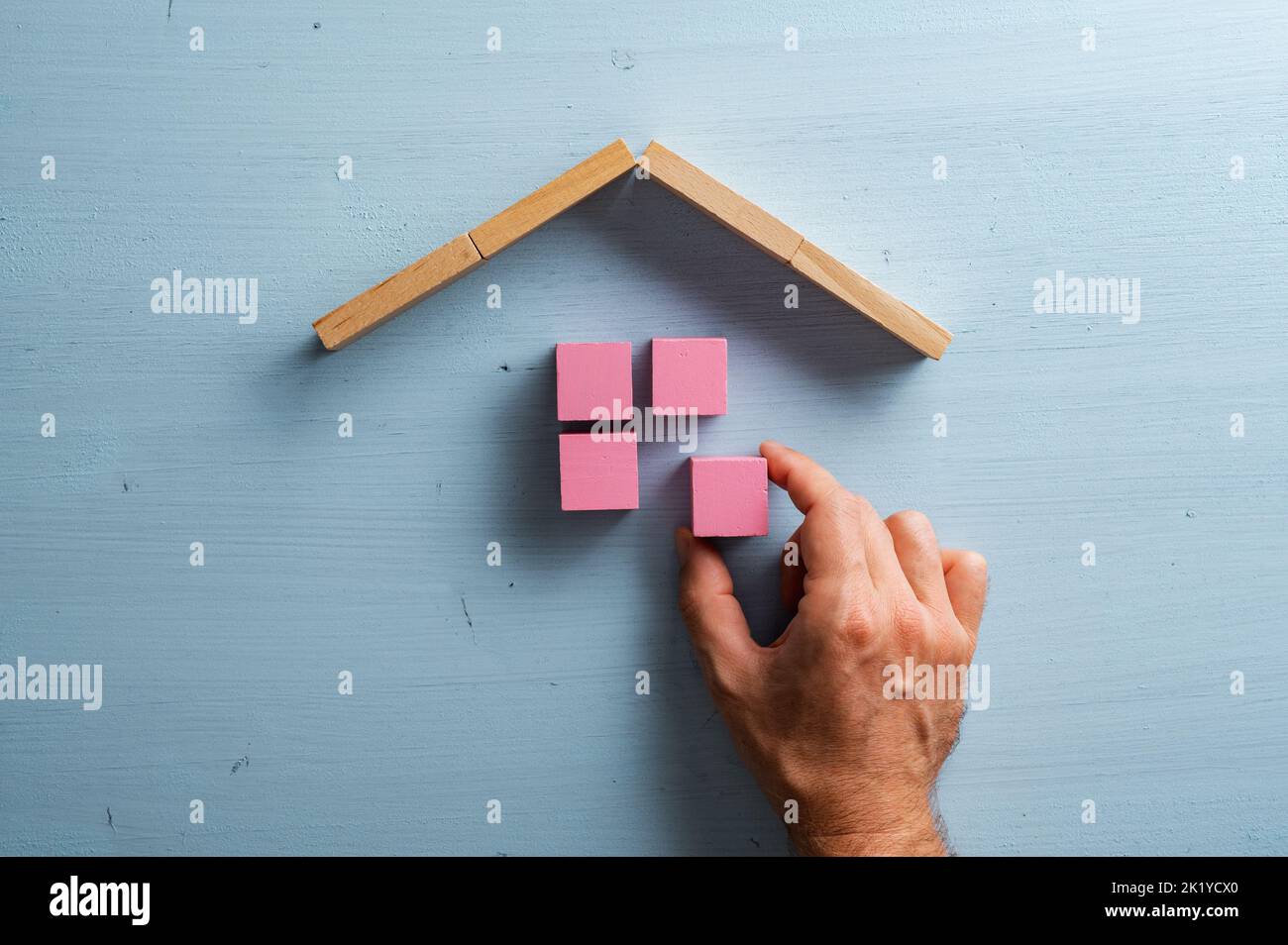 Male hand building a house of pink wooden blocks over blue wooden background. Stock Photo