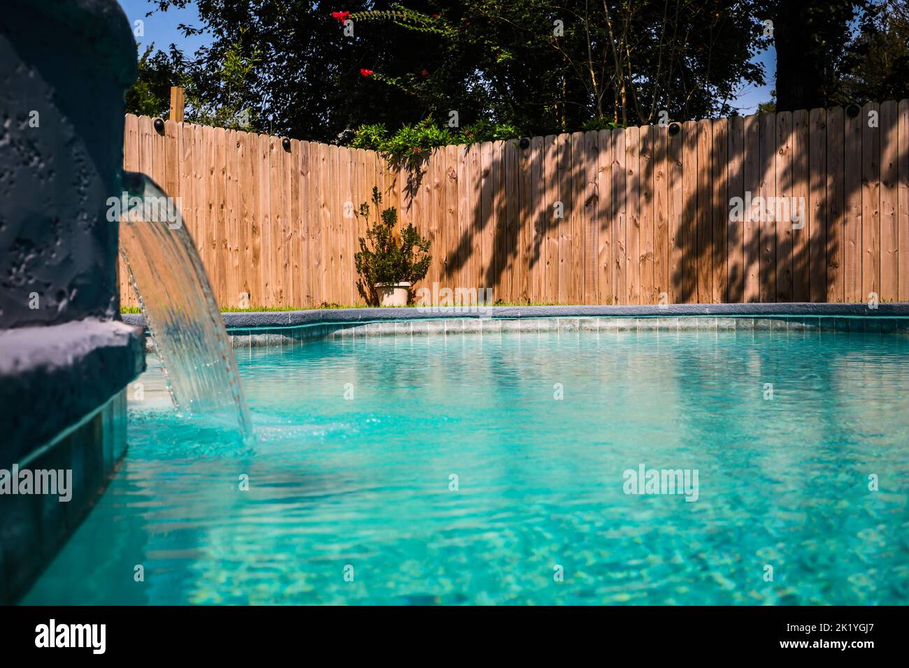 Close up of a gray grey accent swimming pool with turquoise blue water in a fenced in backyard in a suburb neighborhood Stock Photo