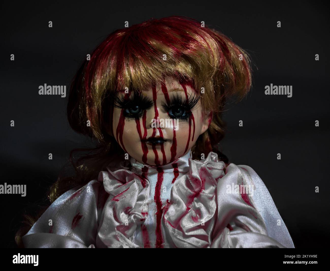 horror style porcelain blonde hair doll face in darkness covered in blood, retro doll style Stock Photo