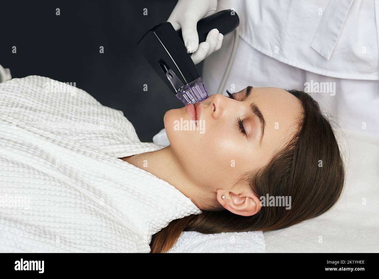 Brunette woman receiving radiofrequency lifting procedure for her face skin rejuvenation at aesthetic cosmetology clinic Stock Photo
