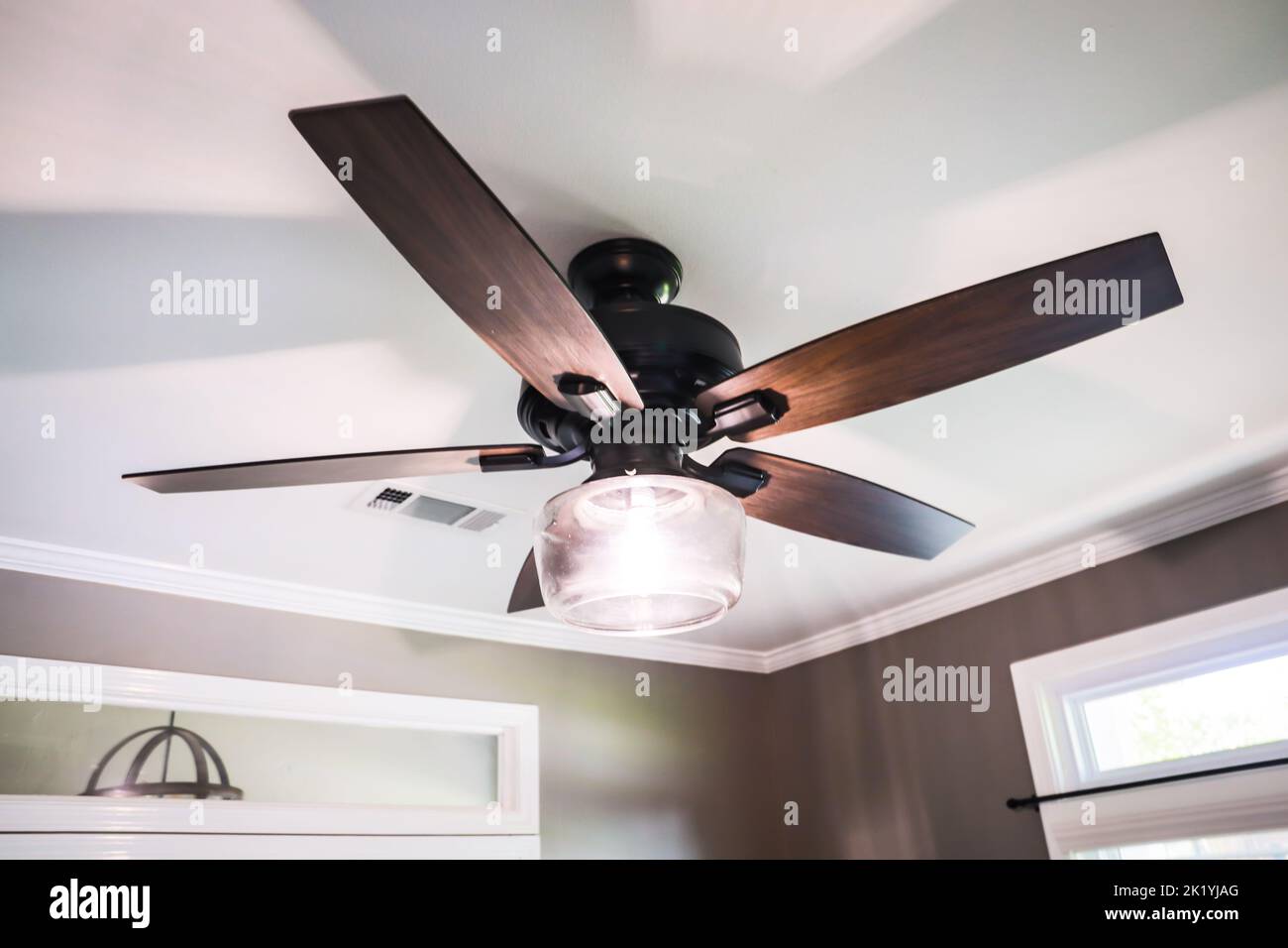 A white tray ceiling with a dark wood modern fan light and brown walls. Stock Photo