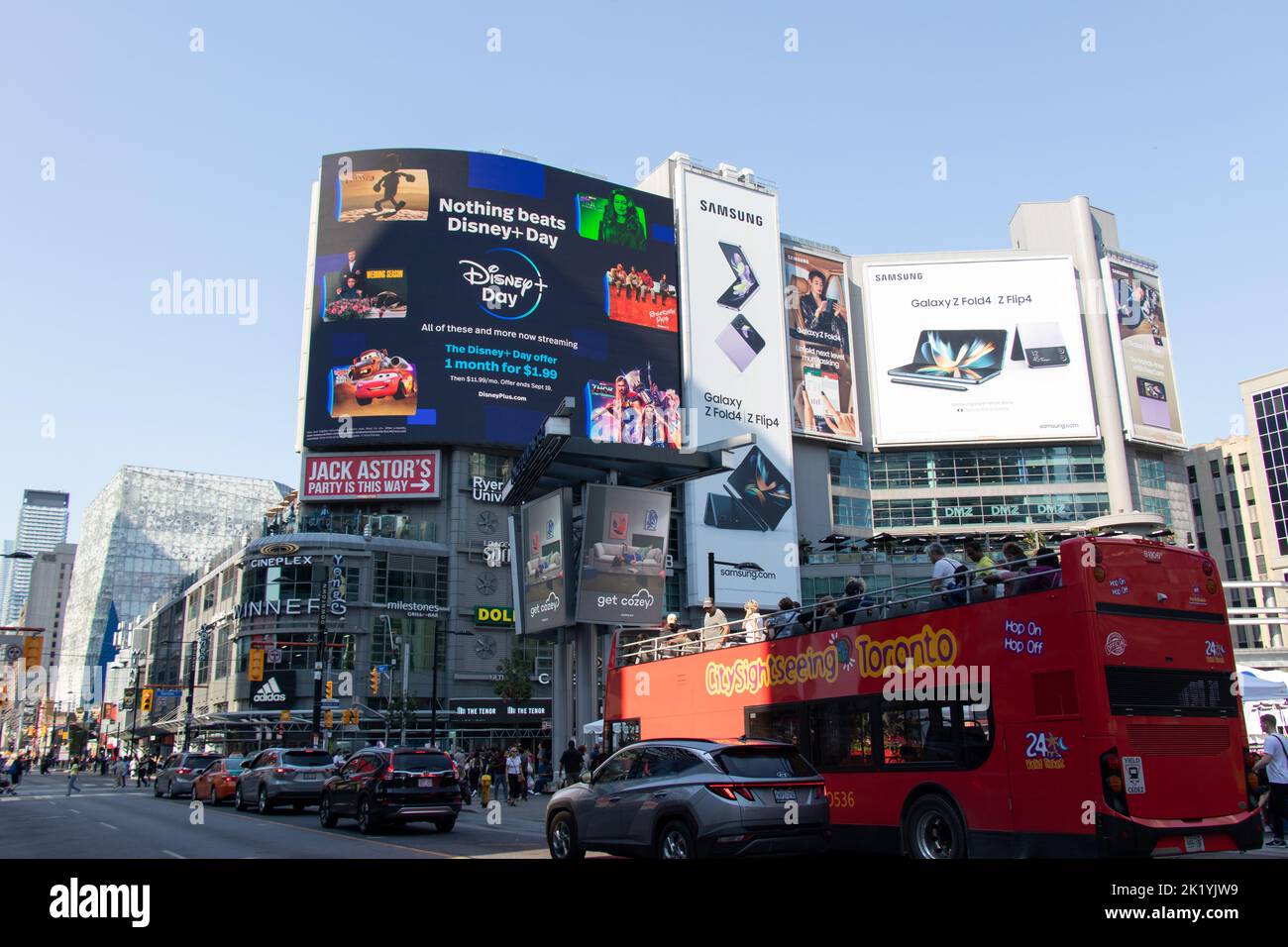 A sightseeing bus passes by Yonge-Dundas Square during a busy, clear sunny day. Stock Photo