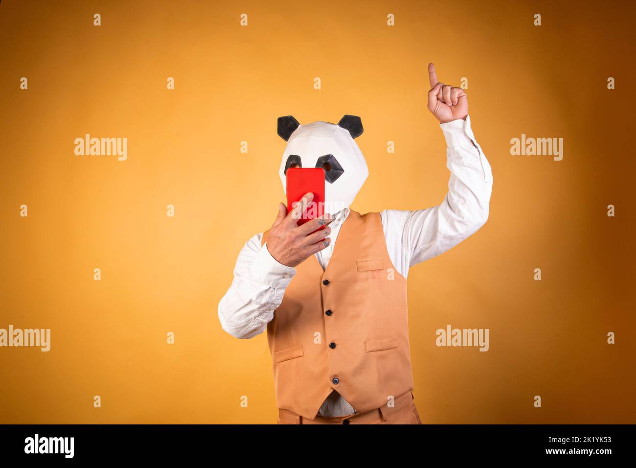 Man in panda bear mask using smartphone and pointing finger on yellow background. Stock Photo