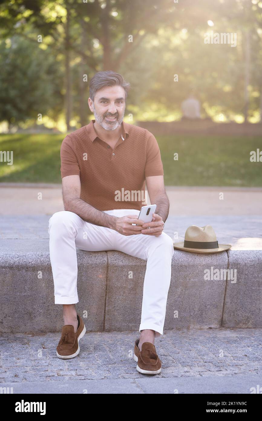 Man looking away and relaxing while using a mobile phone outdoors in a park. Technology concept. Stock Photo
