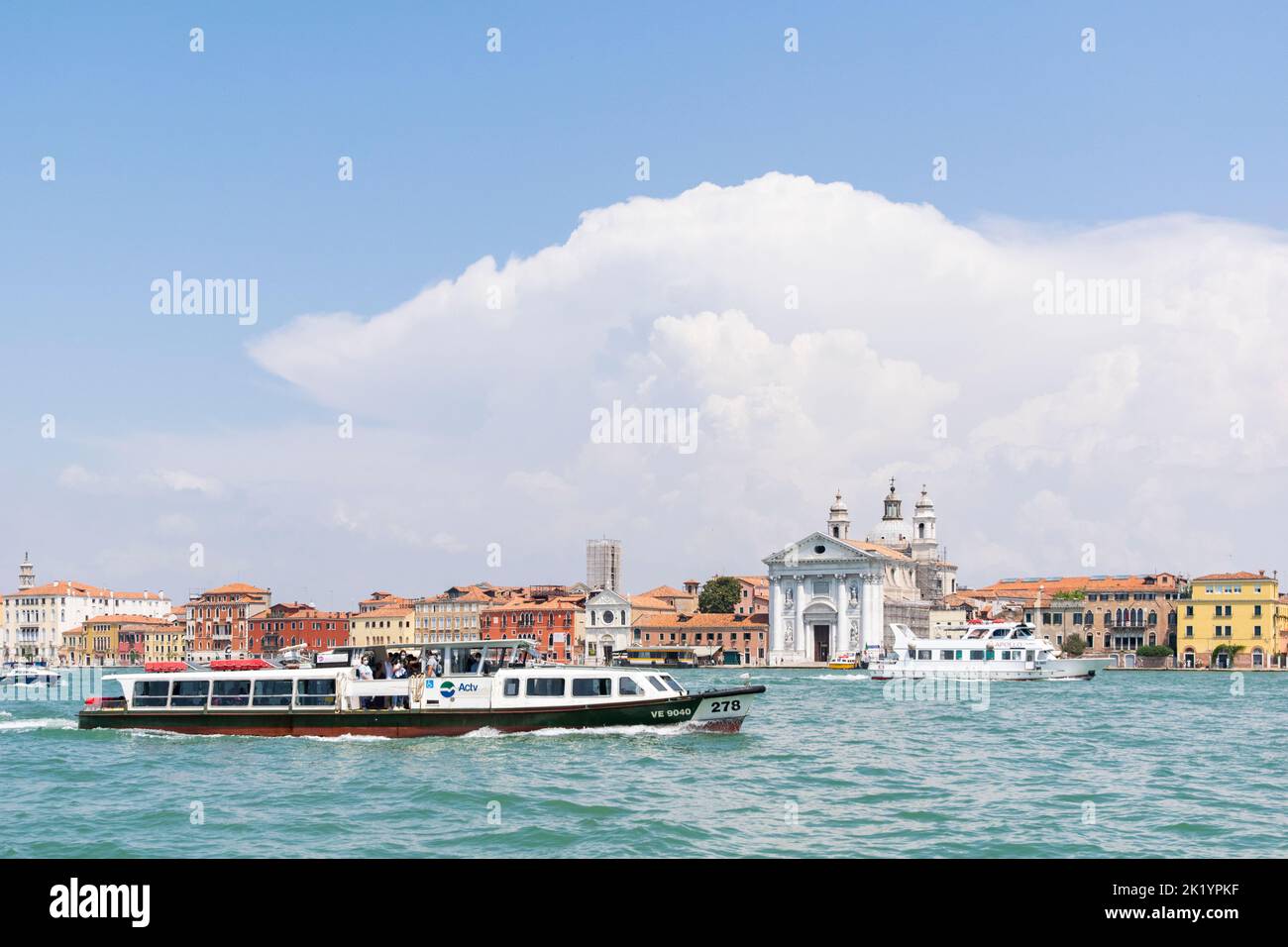 A vaporetto sailing across the Venice big channel in front and the Zattere boat station and Santa Maria del Rosario church in the background, Venice Stock Photo