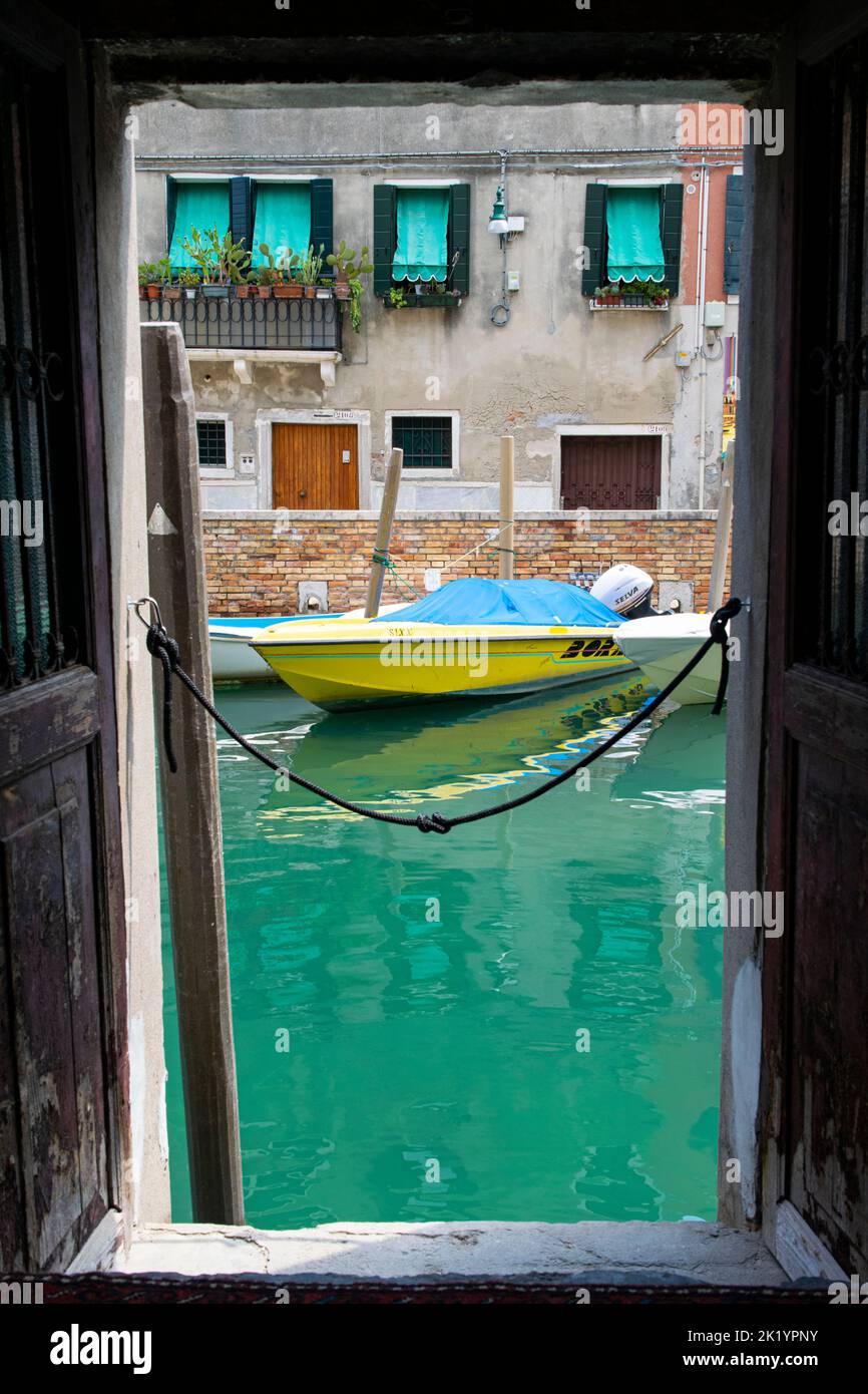a yellow boat parked at a water channel in front of an old house in Arsenale, Venice Stock Photo