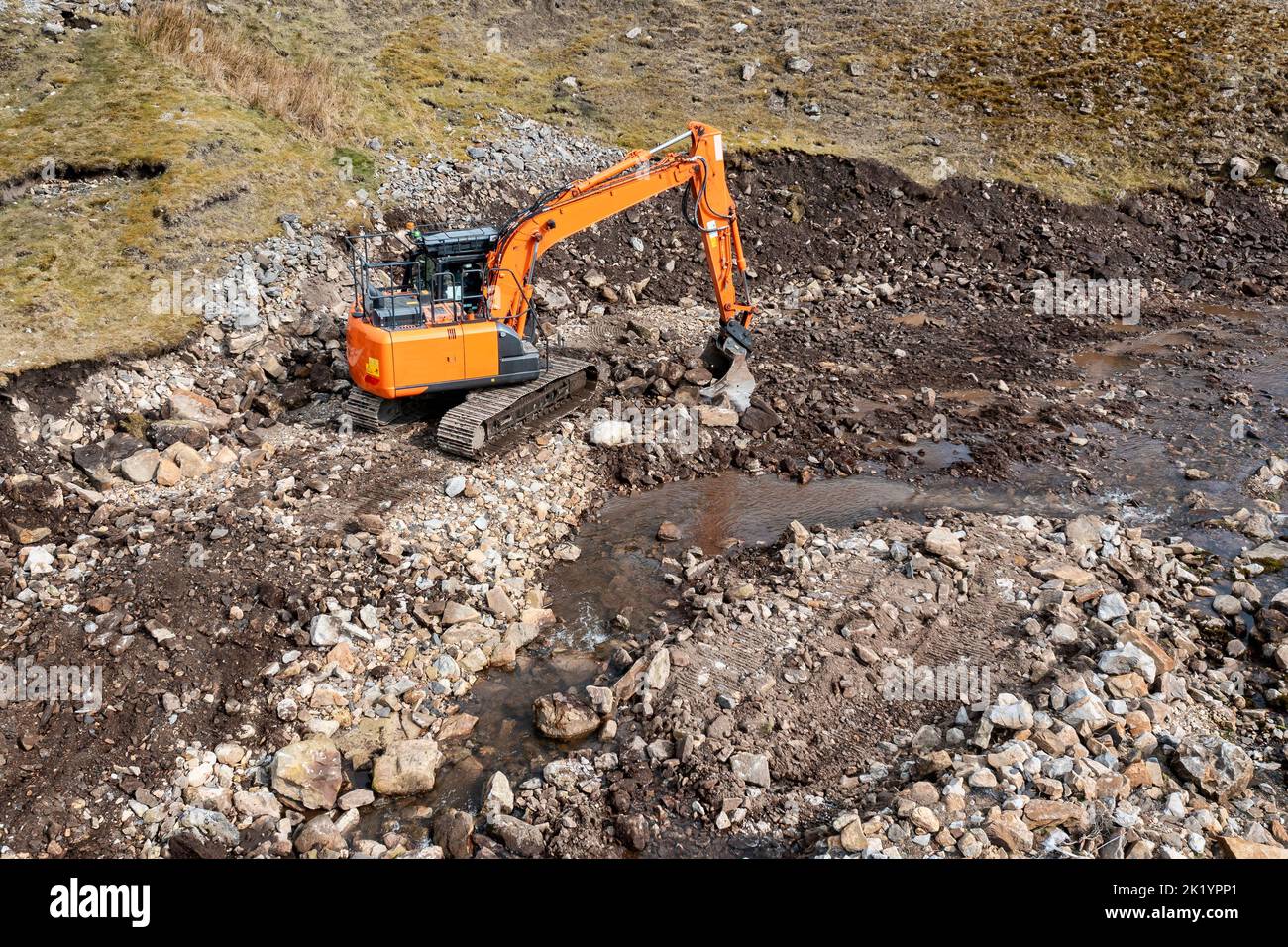 orange hydraulic excavator doing groundwork clearing rocks and stones elevated view Stock Photo