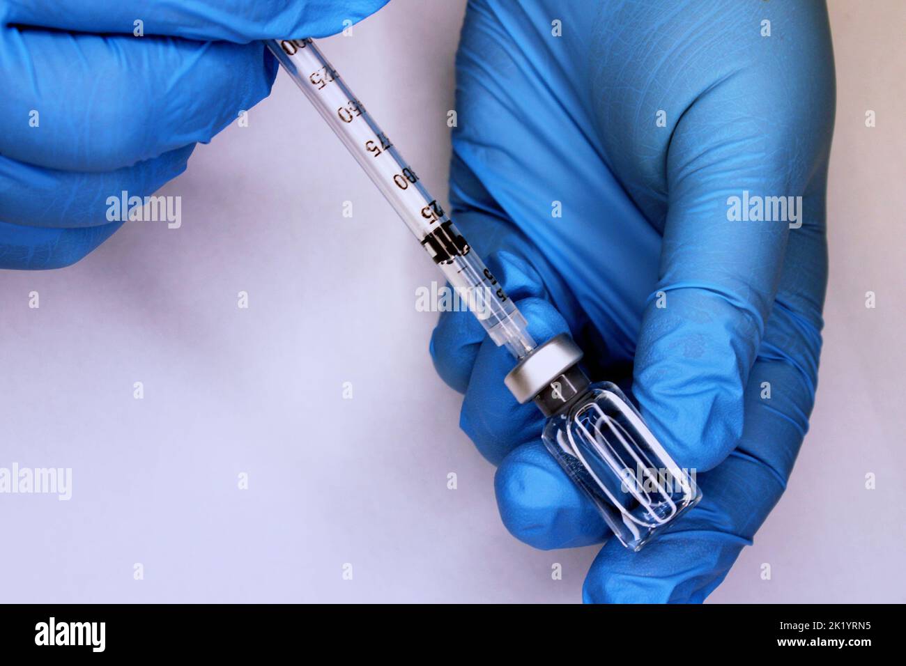 Hands in blue medical gloves close-up drawing up a vaccine from a vial into a syringe. The concept of the fight against Covid19.. Stock Photo
