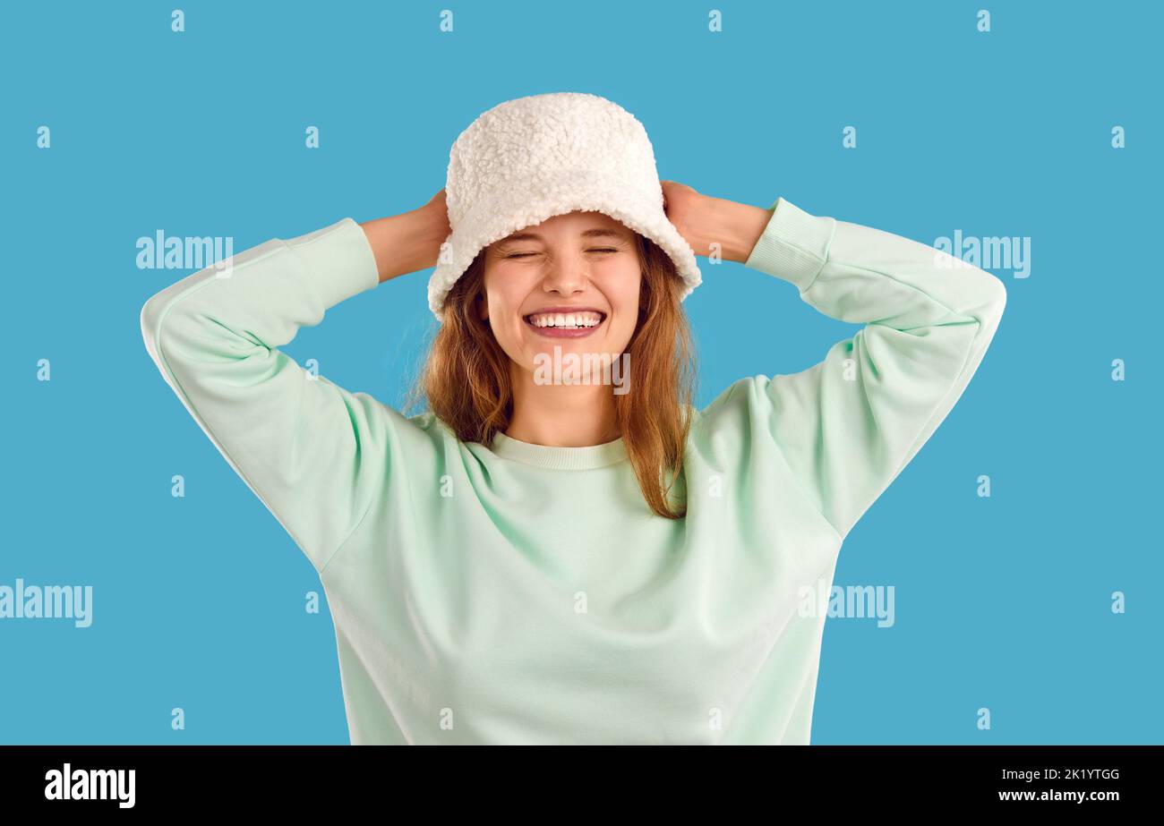 Laughing young woman in white warm hat and mint sweatshirt on light blue background. Stock Photo