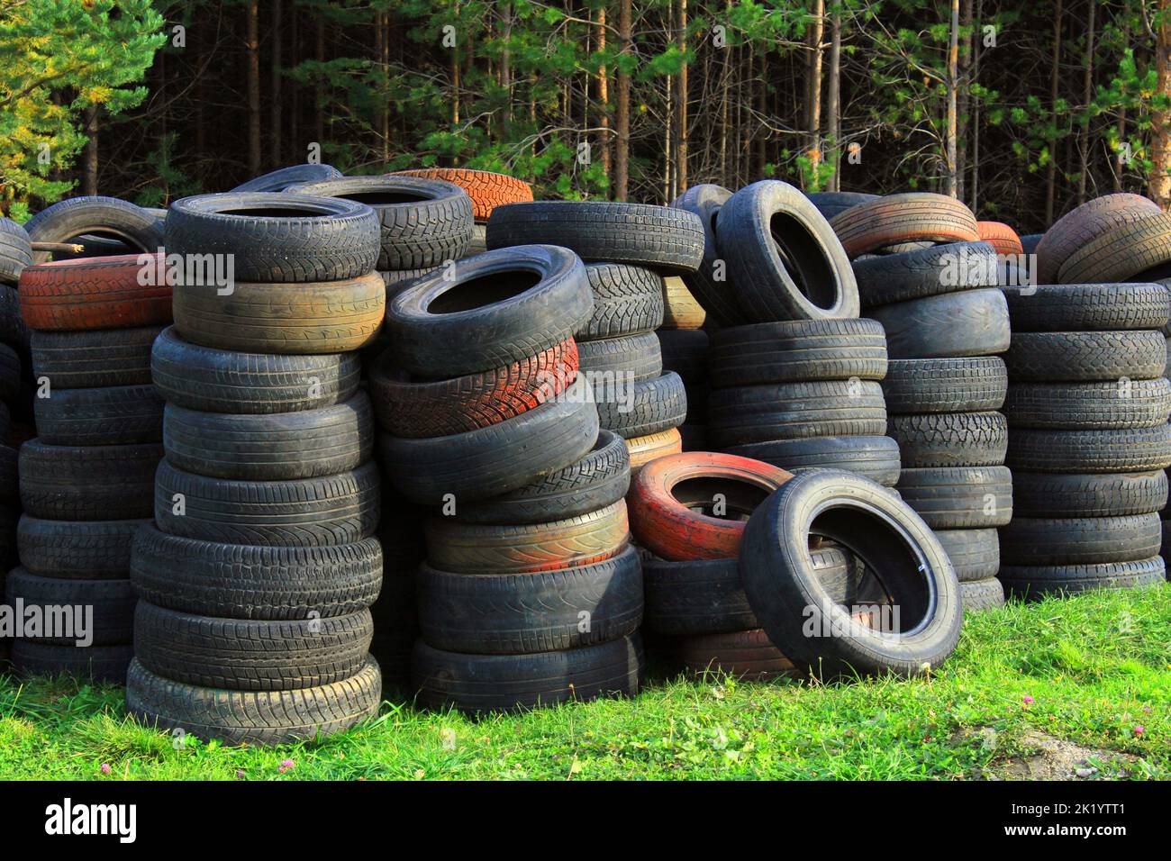 A pile of old car tires lies on the grass against the background of the