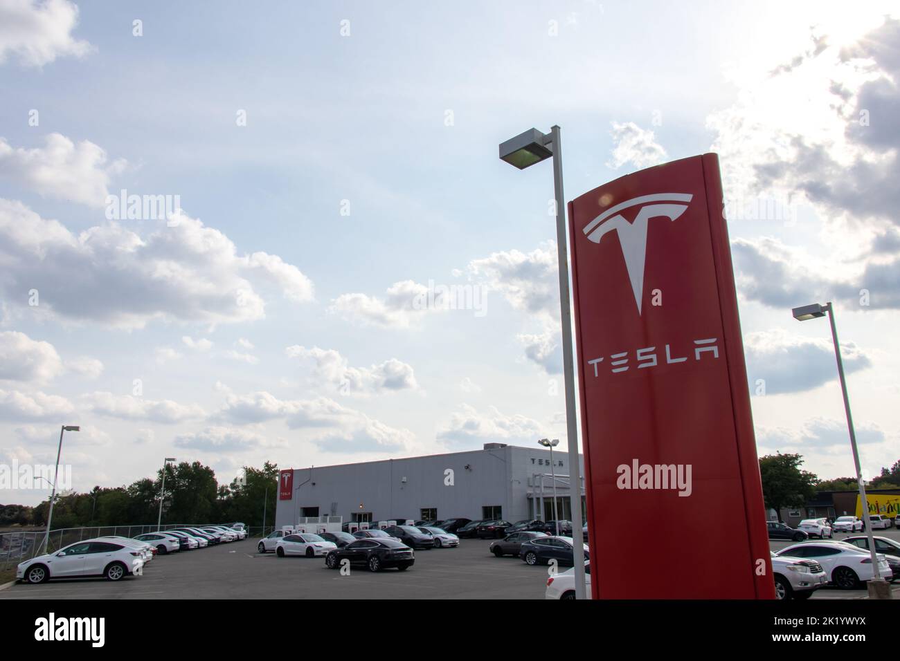 The afternoon sun shines down on a Tesla dealership, Tesla sign out front of a dealer, supercharging location. Stock Photo