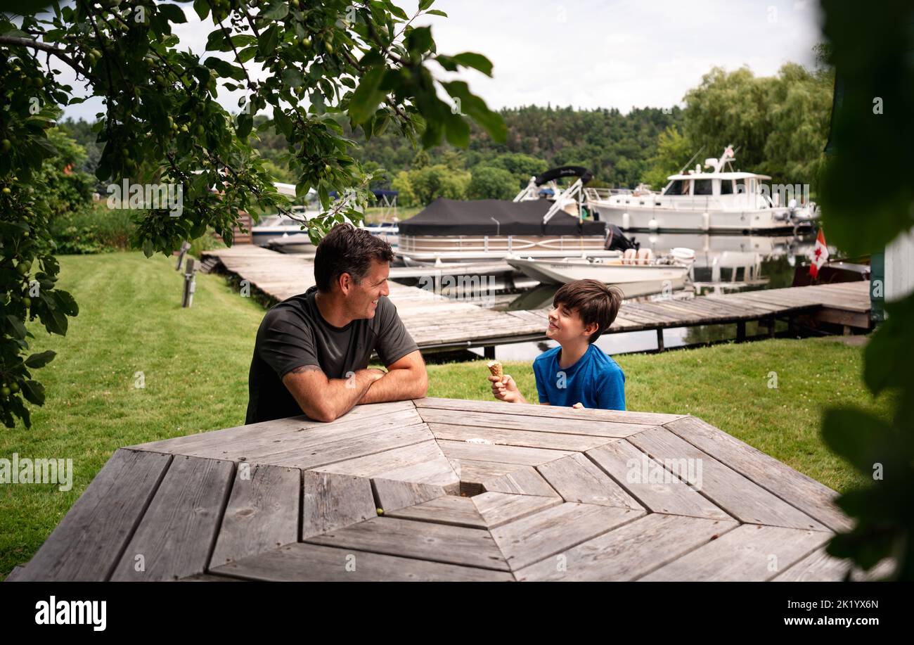 Man and boy eating ice cream cones at picnic table on sunny day. Stock Photo