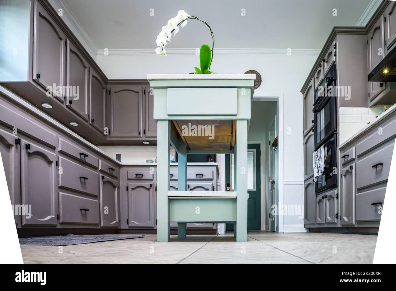 Low angle view of a renovated kitchen in an older home with painted gray cabinets, marble countertops, a small portable island and a tiled floor. Stock Photo