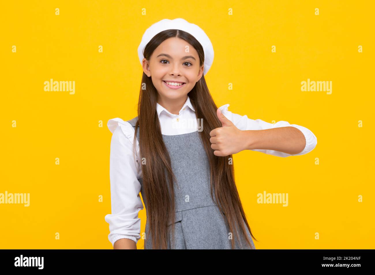 Happy casual teenager child girl showing thumb up and smiling isolated on yellow background. Happy girl face, positive and smiling emotions. Stock Photo