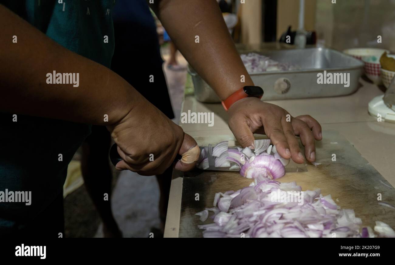 Cook cutting onions on a board in common kitchen of a urban restaurant