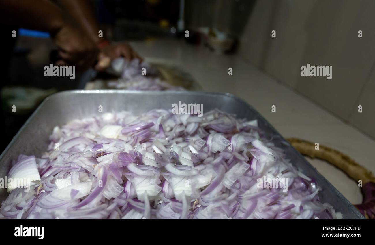 Cook cutting onions on a board in common kitchen of a urban restaurant