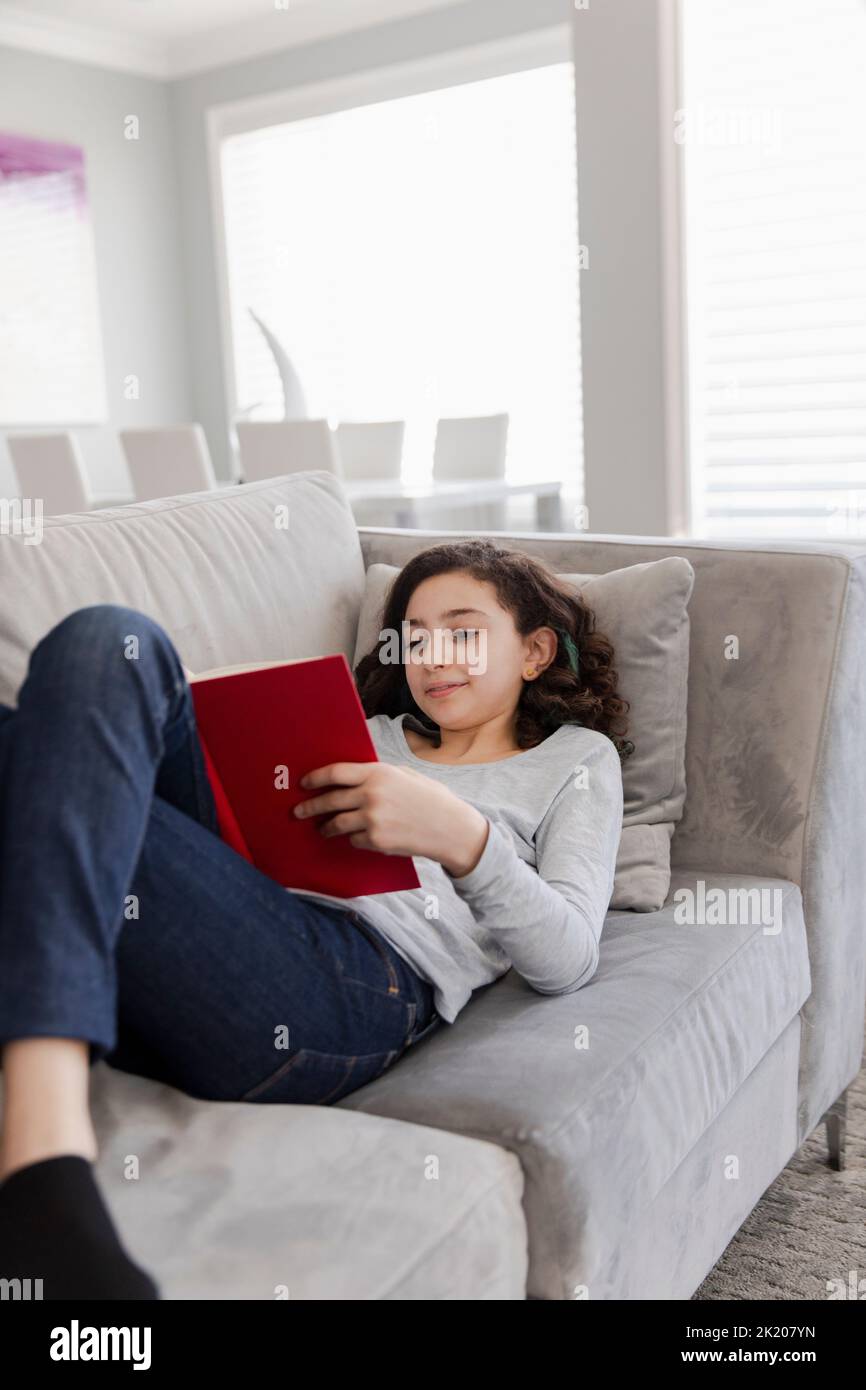 Girl lying on sofa reading Stock Photo Alamy