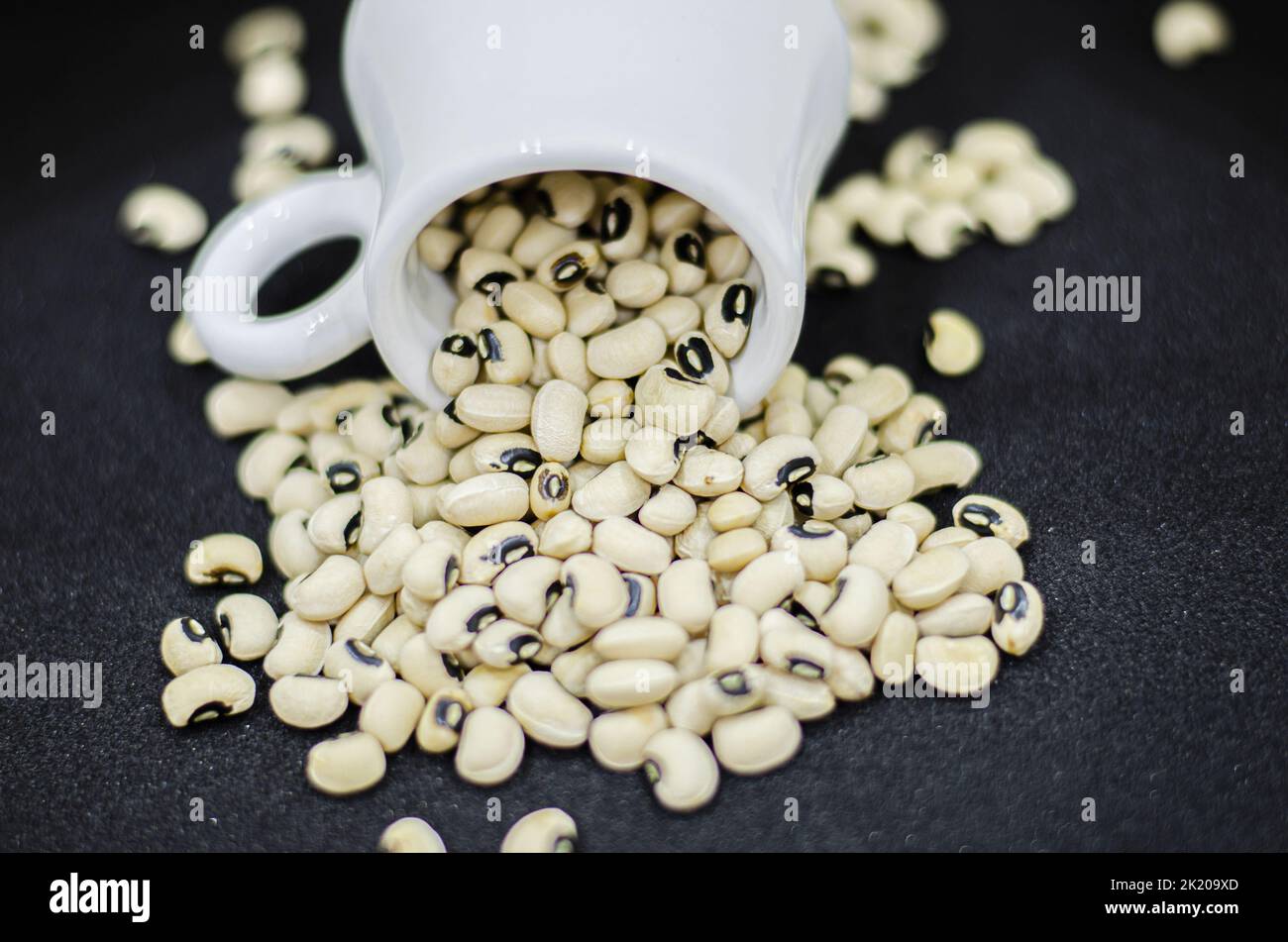 Black eyed beans pouring from a mug on a black background,  dried kidney beans on a black background Stock Photo
