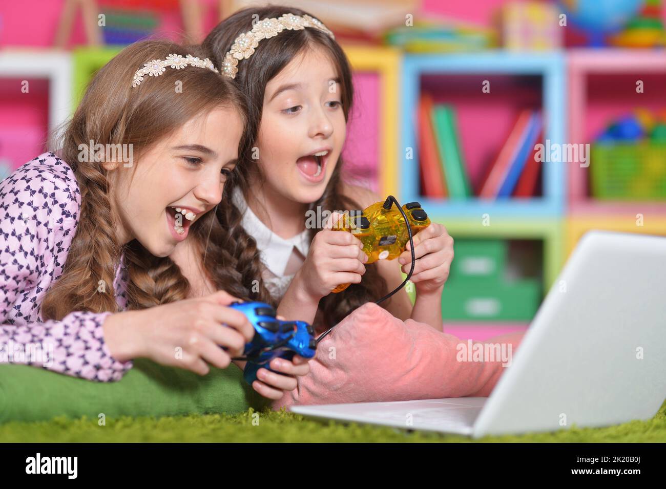 Portrait of two girls playing with joystick and laptop Stock Photo