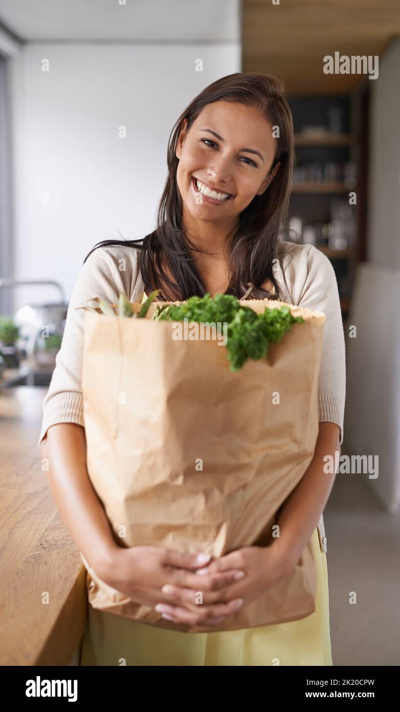 Fresh from the farmers market. A young woman standing in her kitchen holding a bag of groceries - portrait. Stock Photo