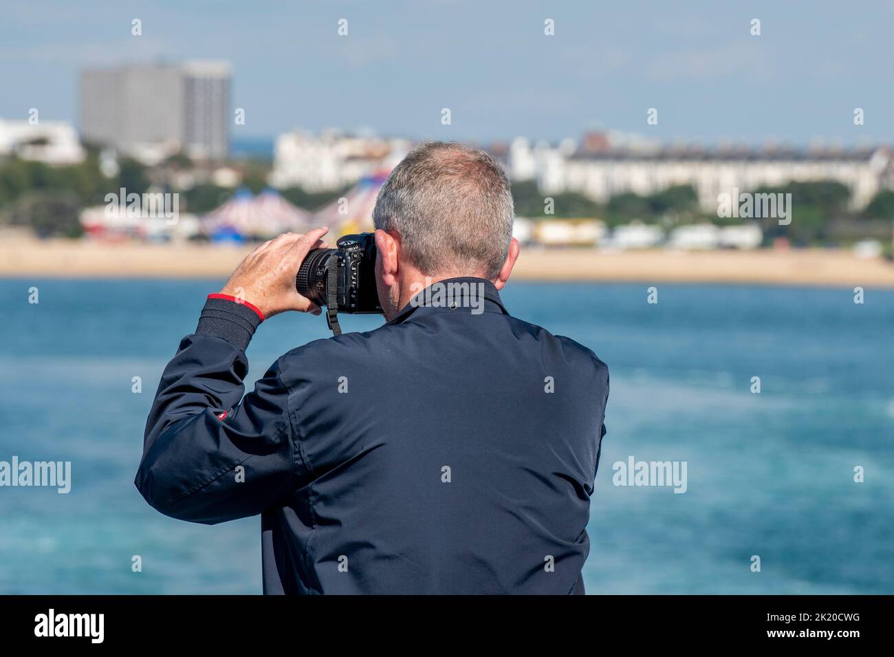 older man taking a photograph using a DSLR camera, photographer using a large camera to take a picture, holiday snaps, travel photography, retirement. Stock Photo
