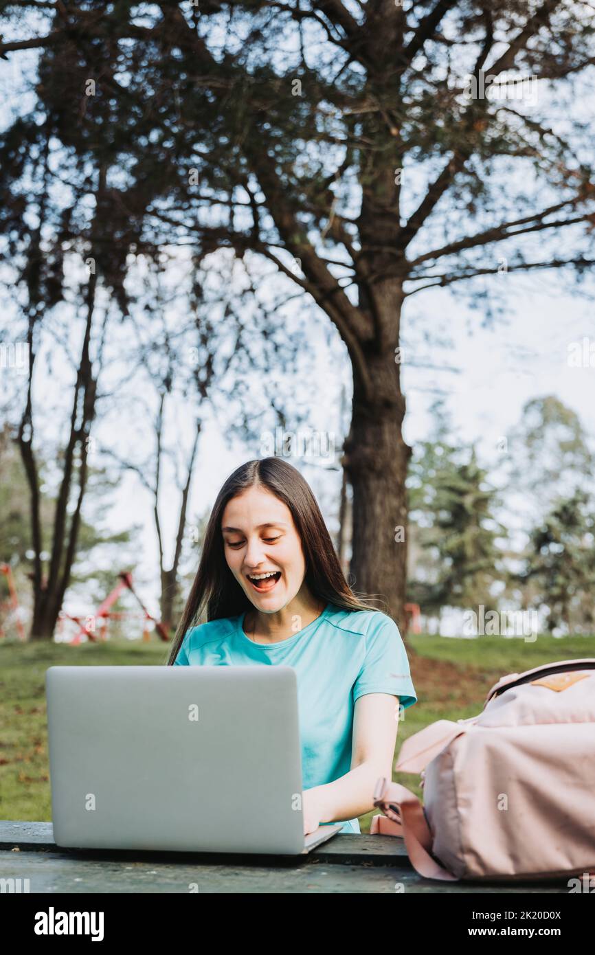 Female university student laughing and using her laptop in college campus park. Turquoise tshirt Stock Photo