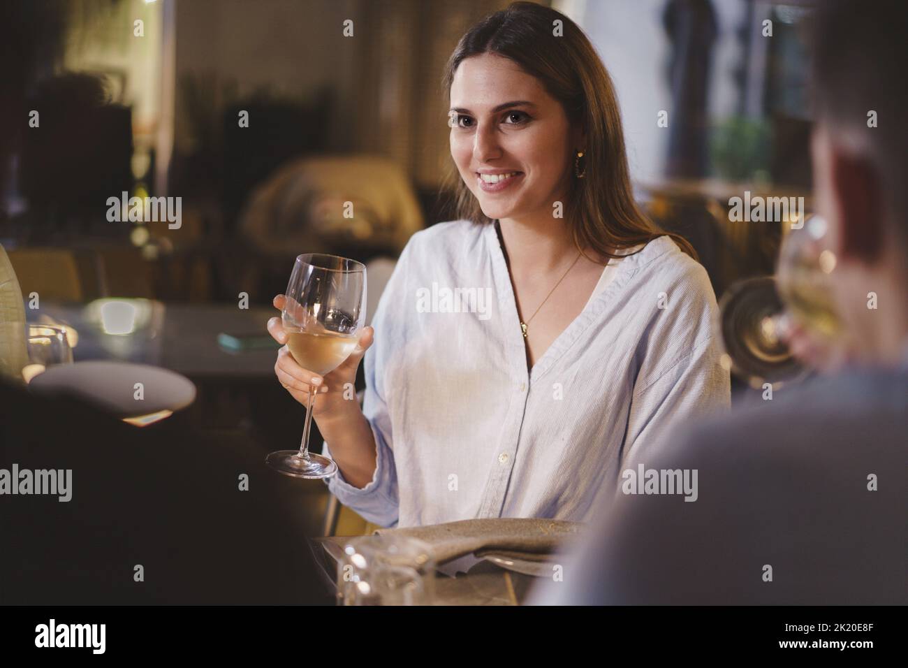 Beautiful young lady carefree enjoying a glass of white wine in an elegant restaurant on a weekend night sitting at a table with her friends - people, Stock Photo