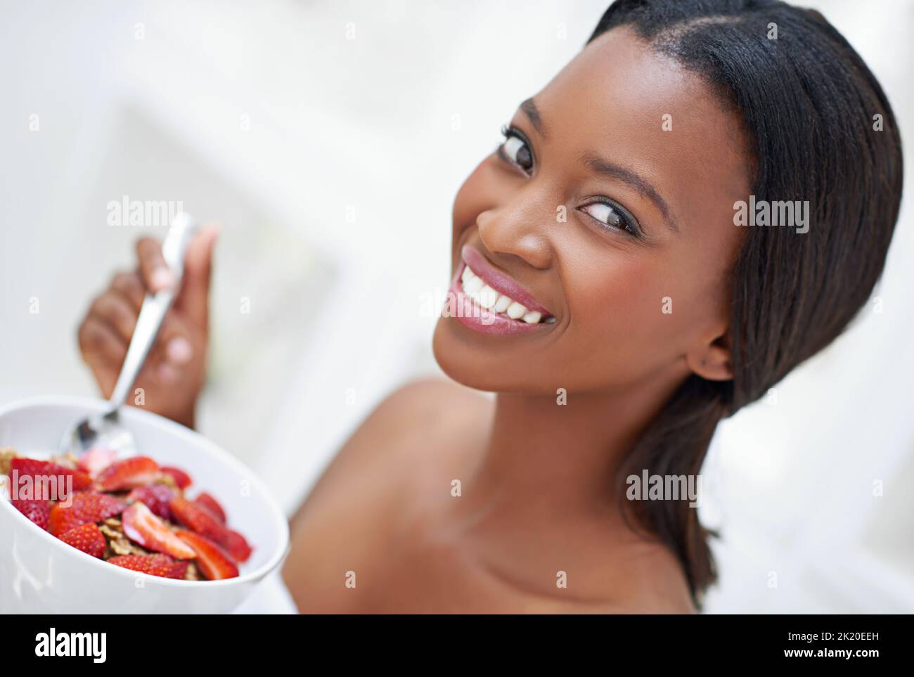 She stands out like a strawberry in a bowl of peas. a beautiful young woman eating strawberries. Stock Photo