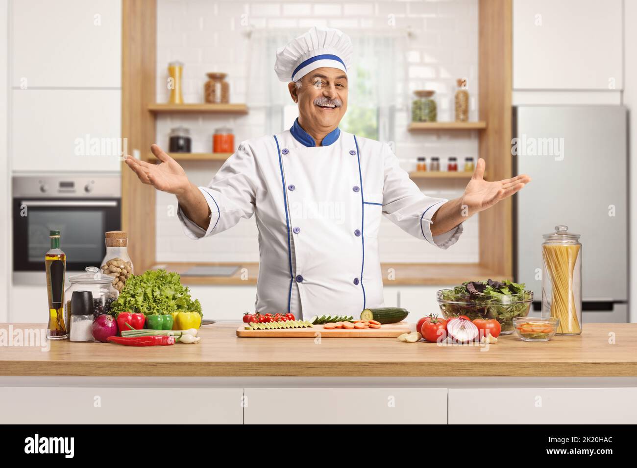 Mature male chef spreading arms behind a kitchen counter and smiling at camera Stock Photo