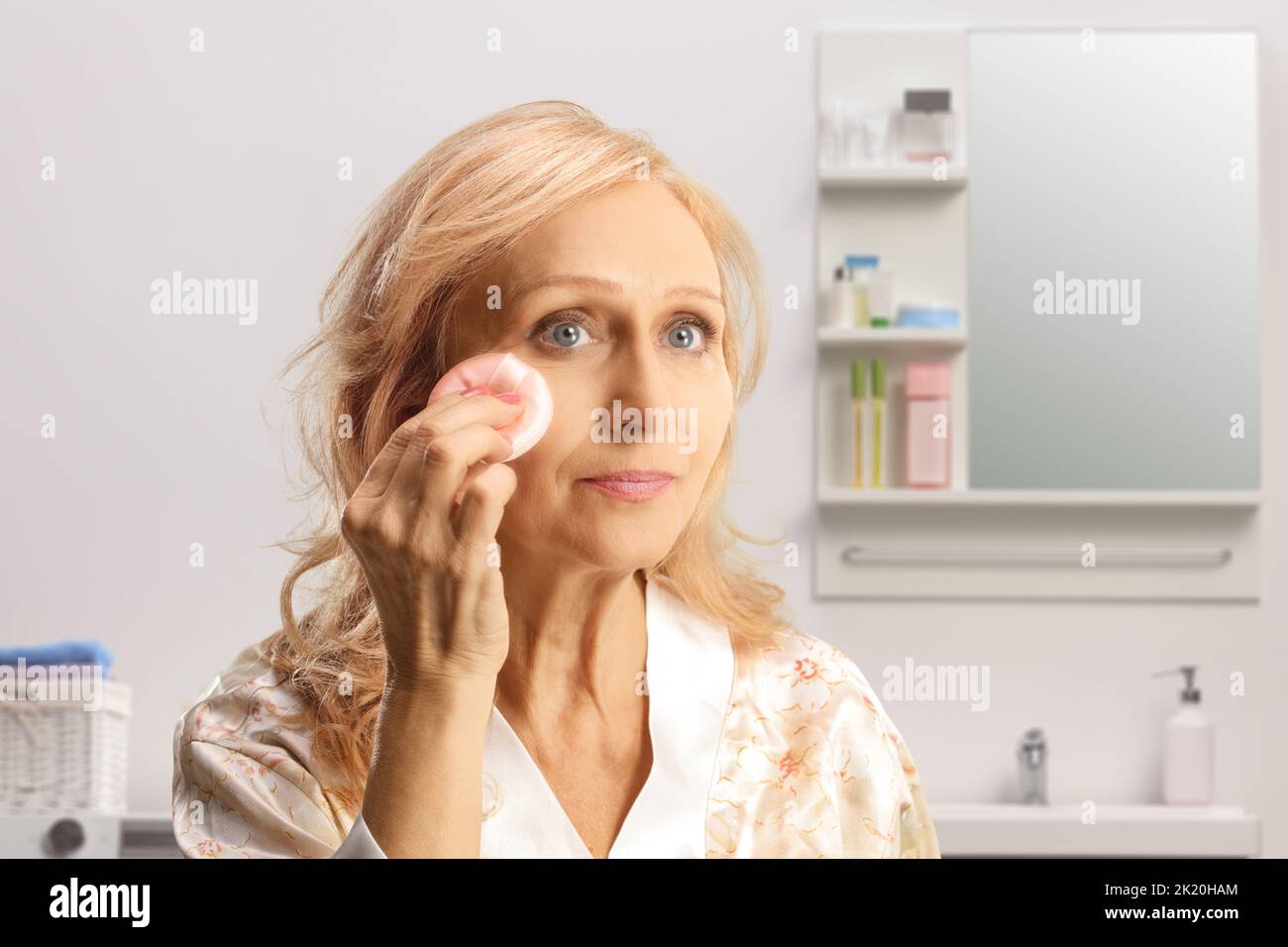Mature woman using a face cotton pad inside a bathroom Stock Photo