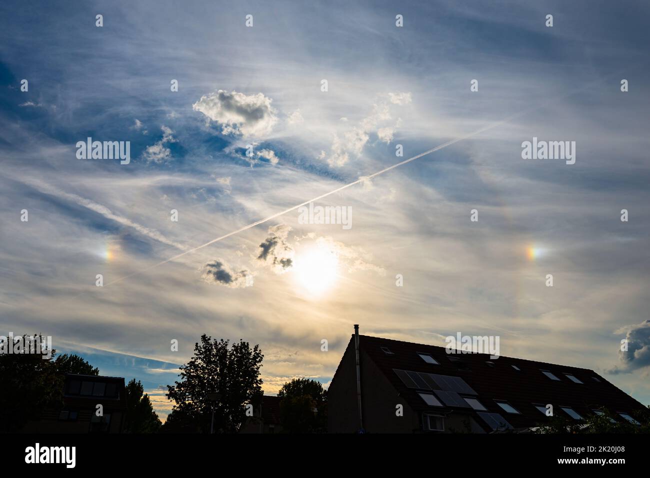 Halo in the sky. Visible is a faint 22-degree circular halo and two bright parhelia on either side of the sun, also known as sun dogs or mock suns. Stock Photo