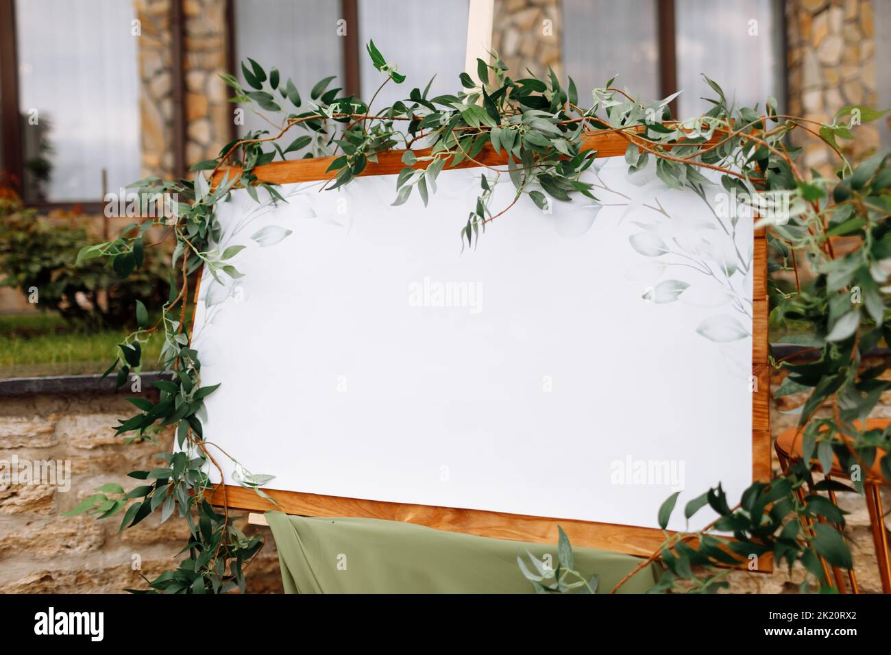 Wedding wooden board, mockup, invitation easel, with white space for an inscription, decorated with fresh greenery and green cloth. Wedding frame outd Stock Photo
