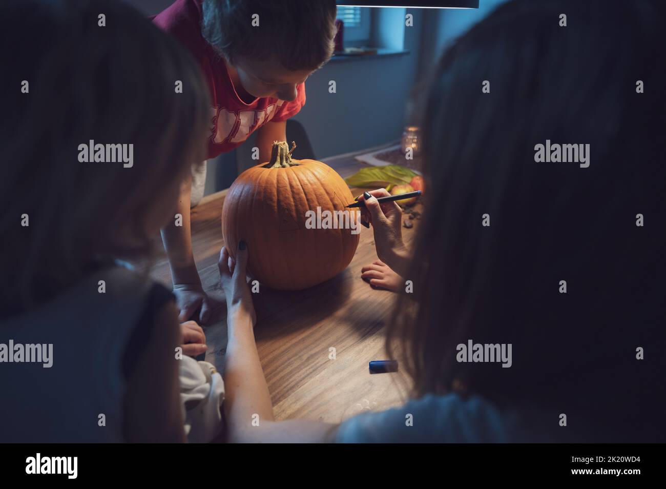 Mother and her three children drawing on a pumpkin to carve it for halloween holidays. Stock Photo