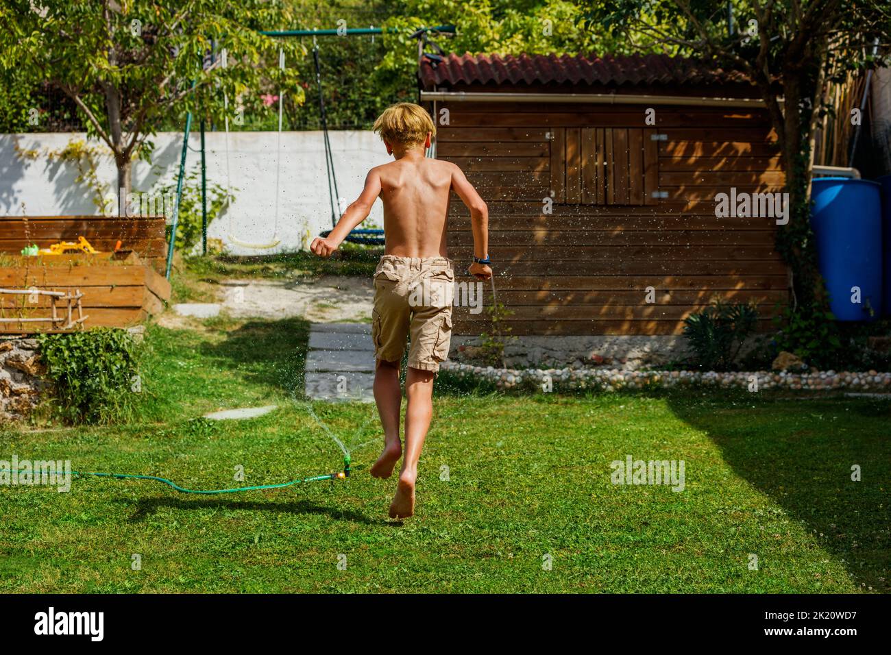 Boy play run around water sprinkler in the garden lawn back view Stock Photo