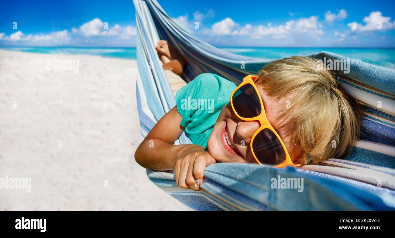 Boy with orange sunglasses lay in hammock on the sea sand beach Stock Photo