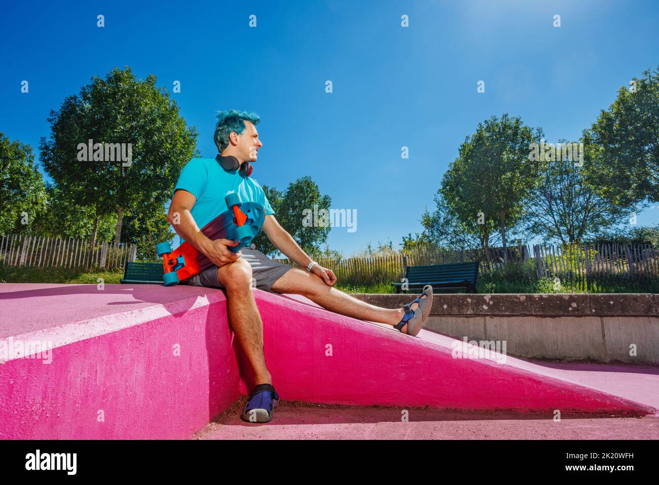 Portrait of a man with blue hair sit holding skateboard in park Stock Photo