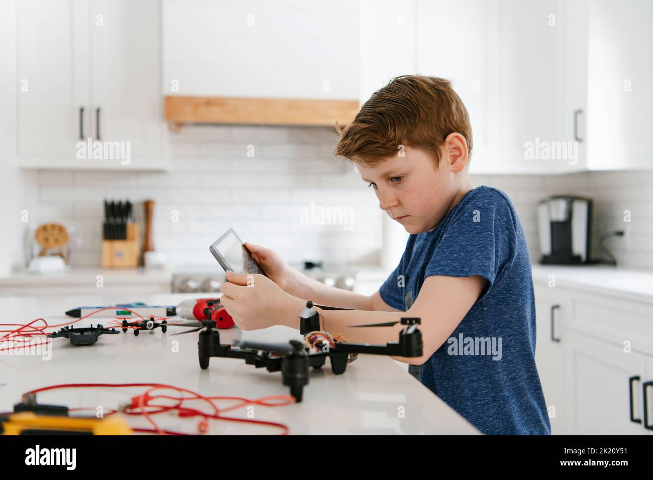 Boy with digital tablet learning to assemble drone at kitchen counter Stock Photo