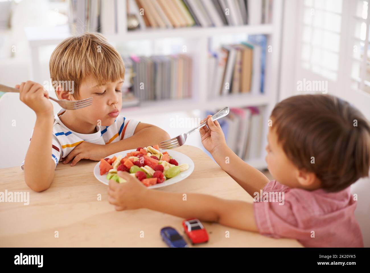 Eating healthy so that we can grow strong. Two adorable little brothers share a bowl of fruit salad at home. Stock Photo