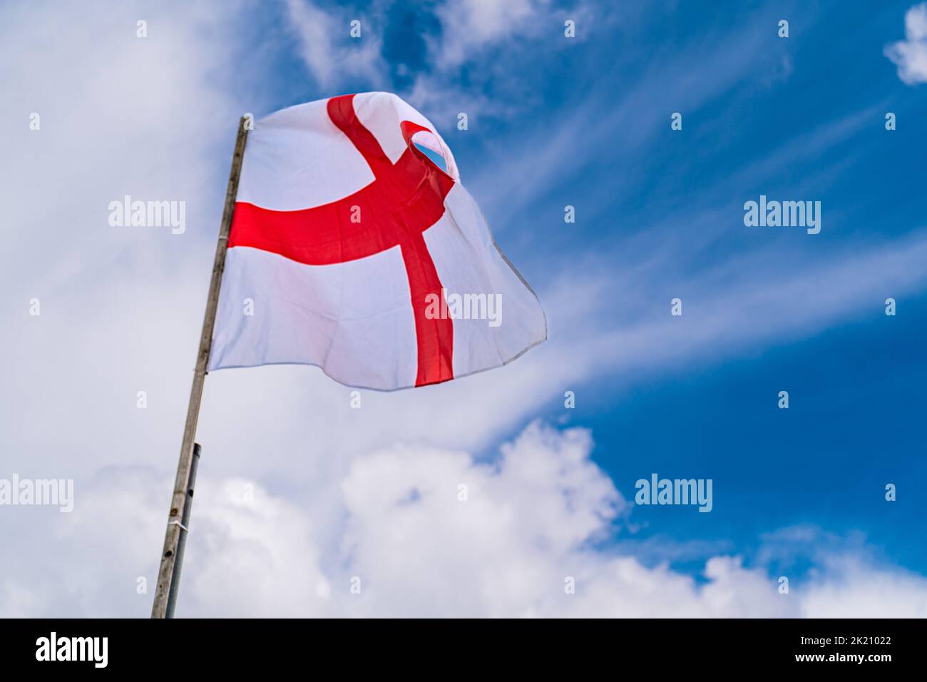 Flag of England on beautiful blue cloudy sky background. White and red flag blowing on the wind. Stock Photo