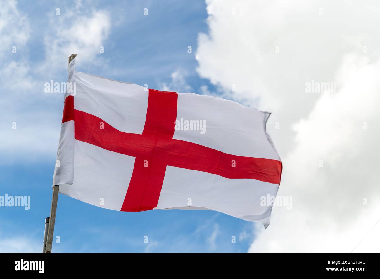 Flag of England on beautiful blue cloudy sky background. White and red flag blowing on the wind. Stock Photo