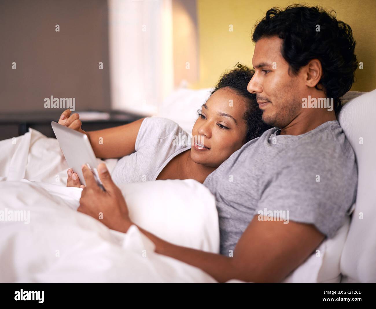 Snuggling while watching our favorite movie. a young couple using a digital tablet while cuddling in bed. Stock Photo