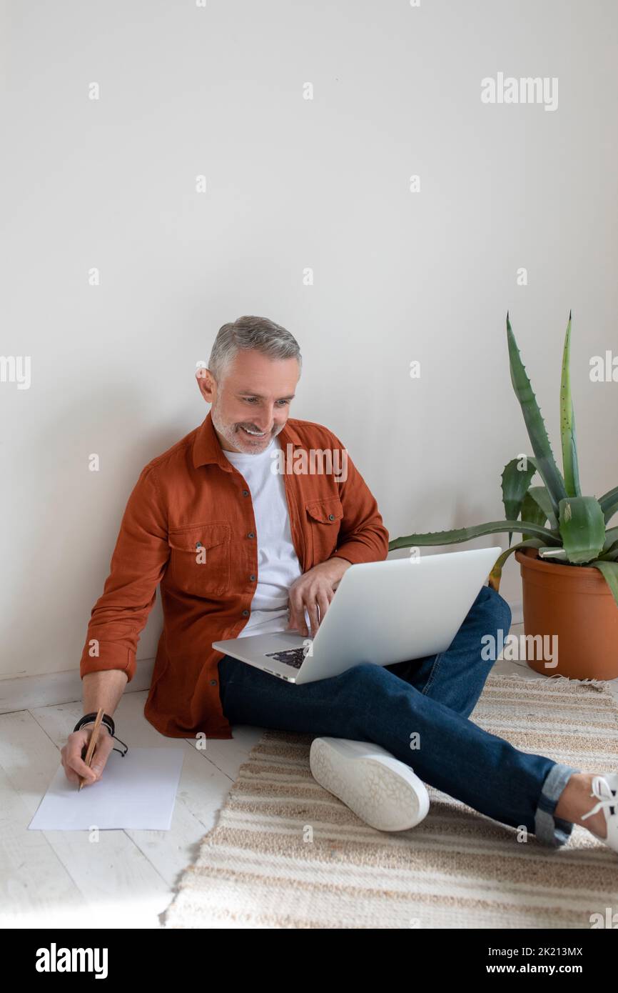 A bearded man in terracotta shirt working on the project and looking involved Stock Photo