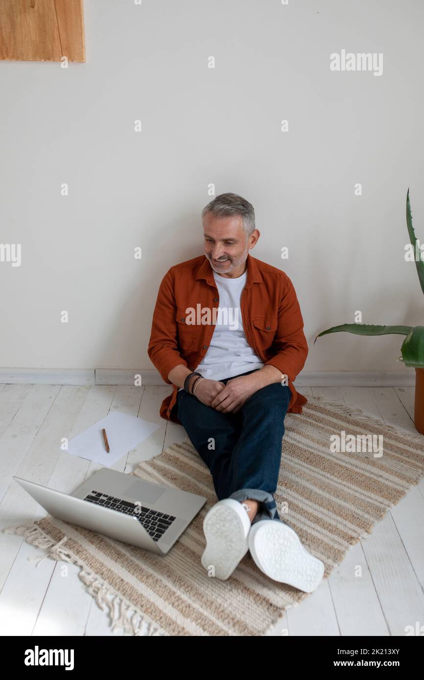 A bearded man in terracotta shirt working on the project and looking involved Stock Photo